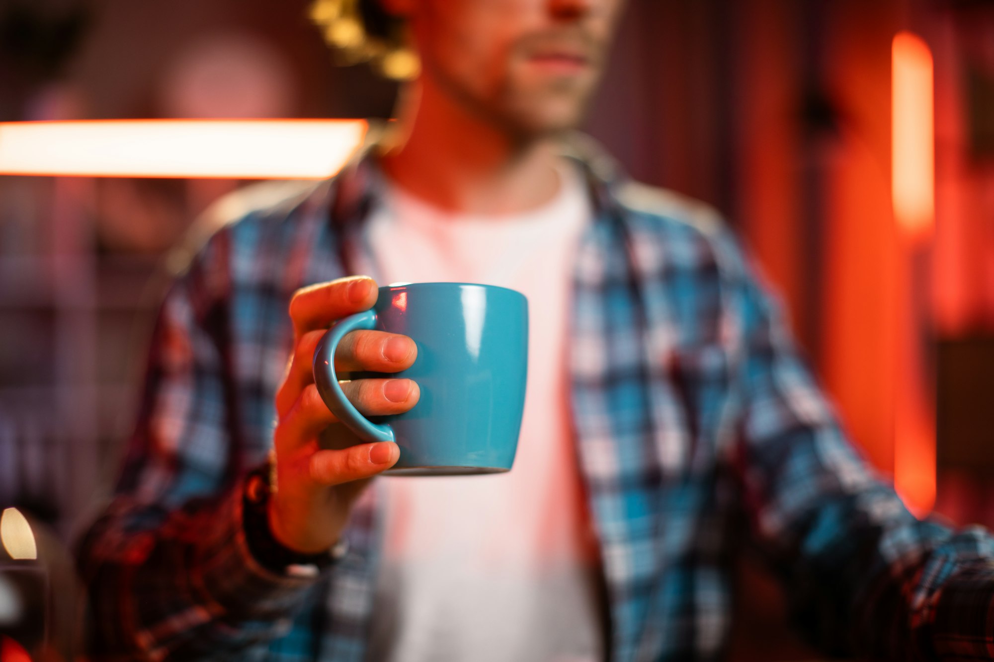 ikable young blond Caucasian man sitting at desk with laptop and hot drink in his hand.